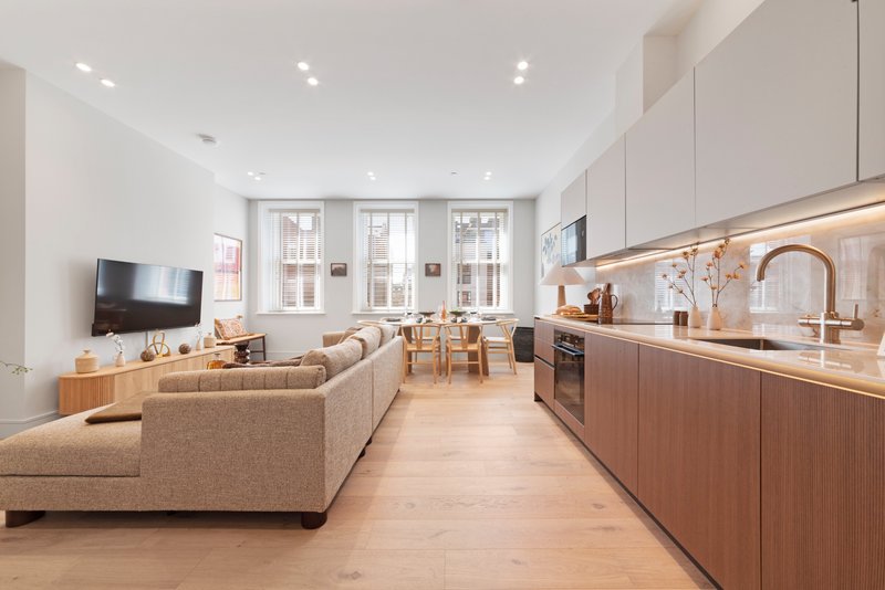 Open-plan kitchen and living area with wooden cabinetry, beige sofa, dining table and bright windows