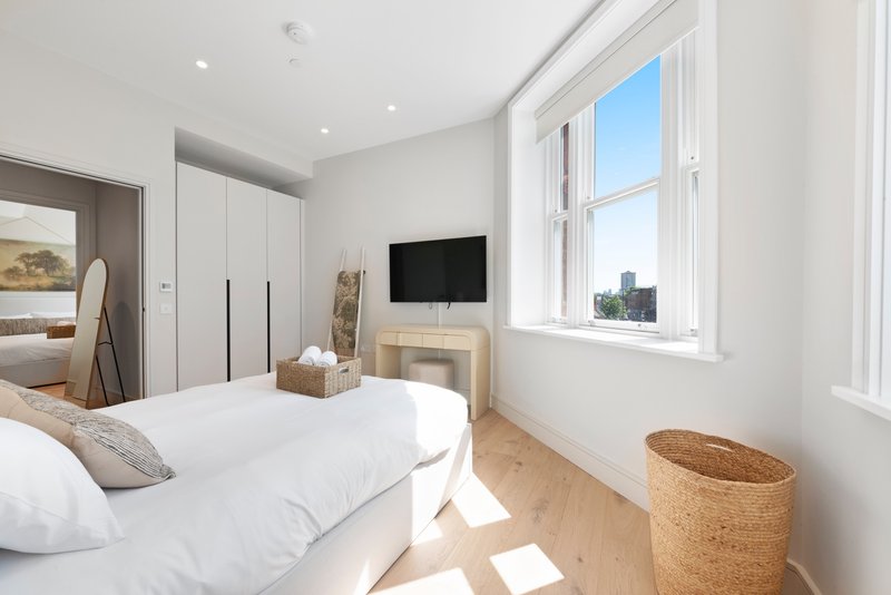 Modern bedroom with white bed, wooden flooring, large windows and city view