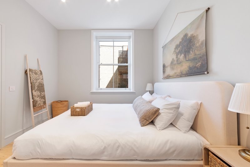 Bright modern bedroom with double bed, white bedding, wooden floor and window view