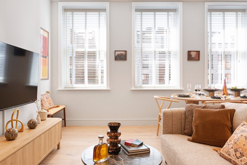 Bright living room with TV, wooden furniture, cream sofa, and large windows with shutters