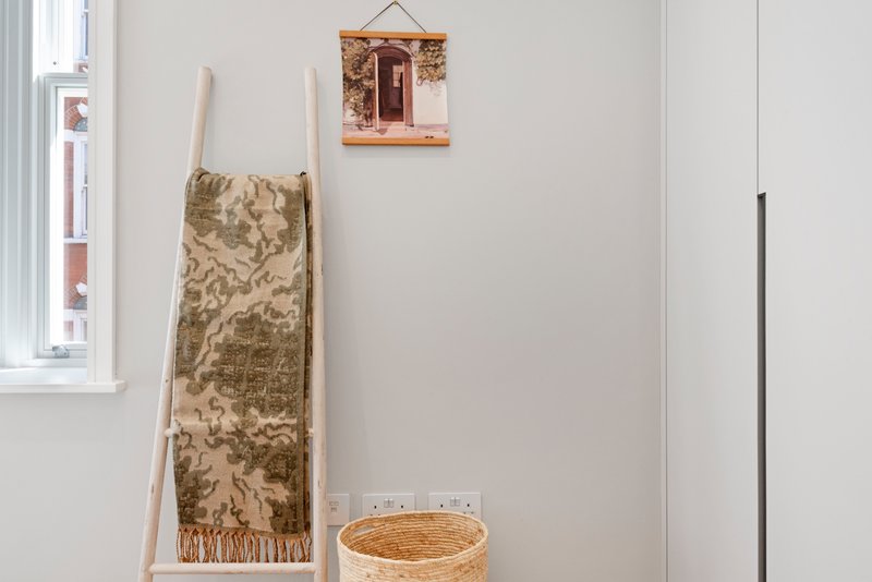 Minimalist bedroom corner with leaning ladder, draped fabric throw, woven basket, and wall art
