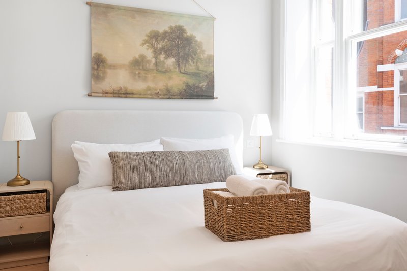 Bright bedroom with double bed, woven storage basket, wooden nightstands and landscape artwork