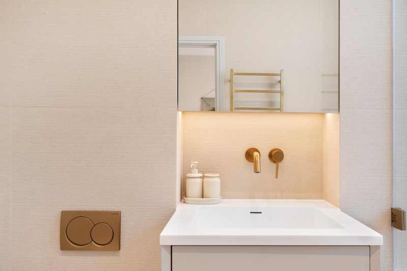 Modern bathroom with white sink, illuminated mirror, bronze faucet, and minimal décor