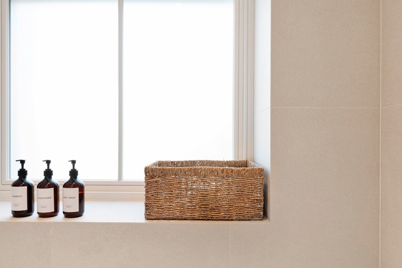 Bathroom windowsill with woven basket and three black pump bottles