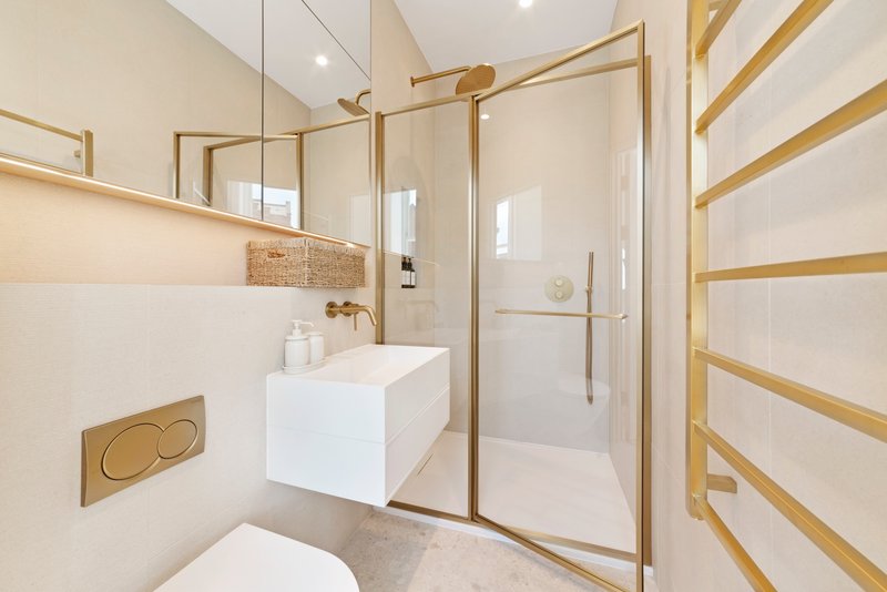 Modern bathroom with white vanity, brass fixtures, walk-in shower and heated towel rail