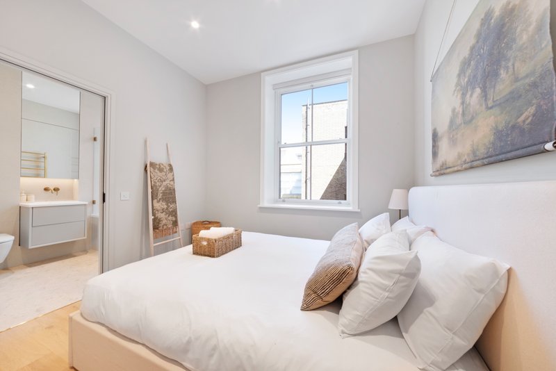 Modern bedroom with double bed, white pillows, woven cushions, and ensuite bathroom visible