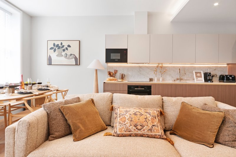 Open-plan living area with beige sofa, dining table, and modern kitchen with white cabinetry