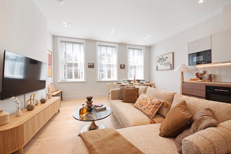 Modern living room with beige sofa, wooden TV unit, kitchen area and large windows