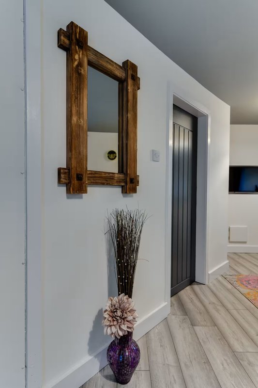 Hallway with wooden-framed mirror, decorative vase with dried flowers, and doorways