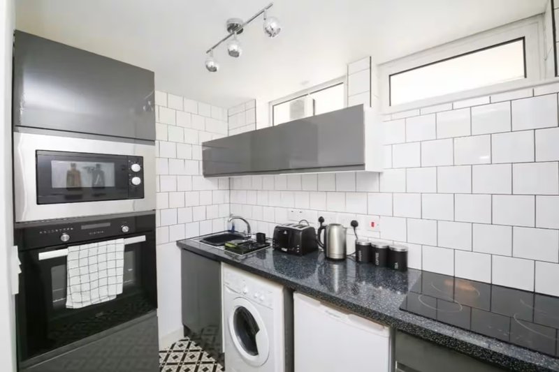 Modern kitchen with white subway tiles, black appliances, washing machine and dark countertops