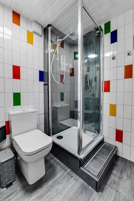 Modern bathroom with colorful tile wall art, glass shower enclosure and white toilet