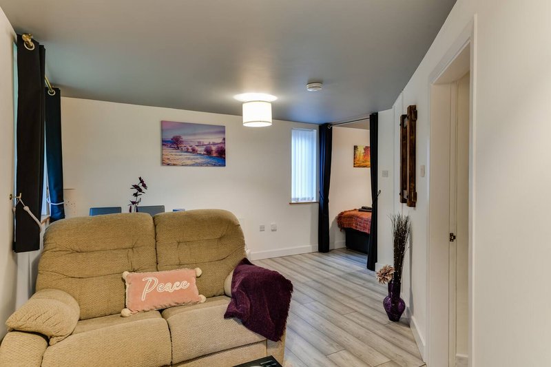 Open-plan living area with gold sofa, framed landscape art, wooden flooring and bedroom visible beyond
