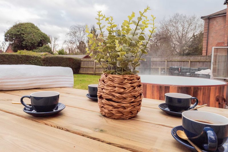 Outdoor wooden table with wicker planter, yellow flowers, and black cups in garden setting