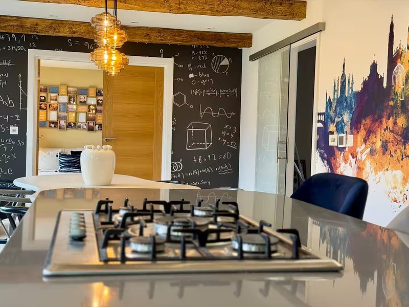 Open-plan kitchen and study area with gas cooktop, chalkboard wall, wooden beams and pendant lighting