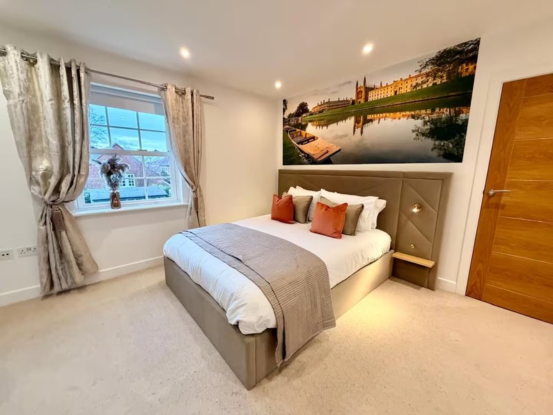 Modern bedroom with double bed, landscape artwork, window with curtains and wooden door