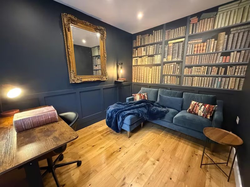 Dark blue living room with bookshelves, sofa, wooden tables, mirror and hardwood flooring