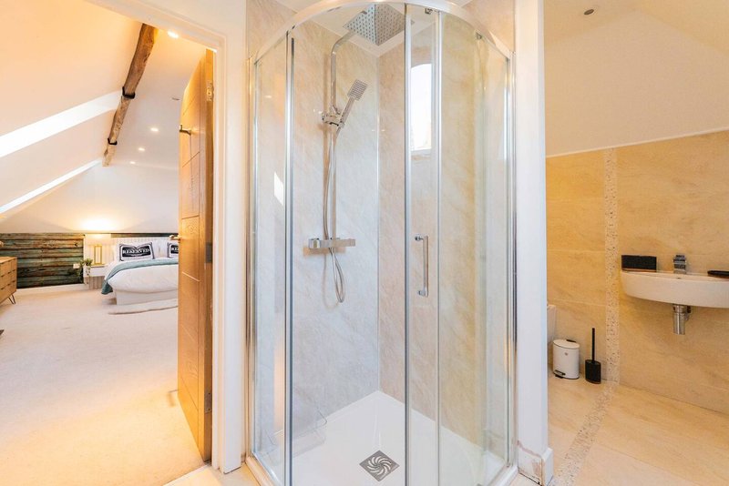 Modern bathroom with glass shower enclosure, golden tiled walls, and bedroom visible through open door