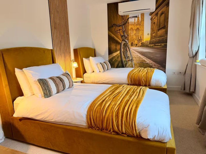 Twin bedroom with mustard-yellow upholstered beds, striped cushions, and street scene wall art
