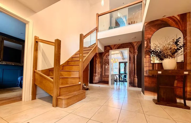 Spacious entrance hallway with wooden staircase, tiled floor and decorative mirror