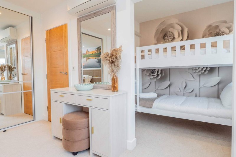 Bright bedroom with white vanity, mirror, bunk bed with white frame and neutral bedding