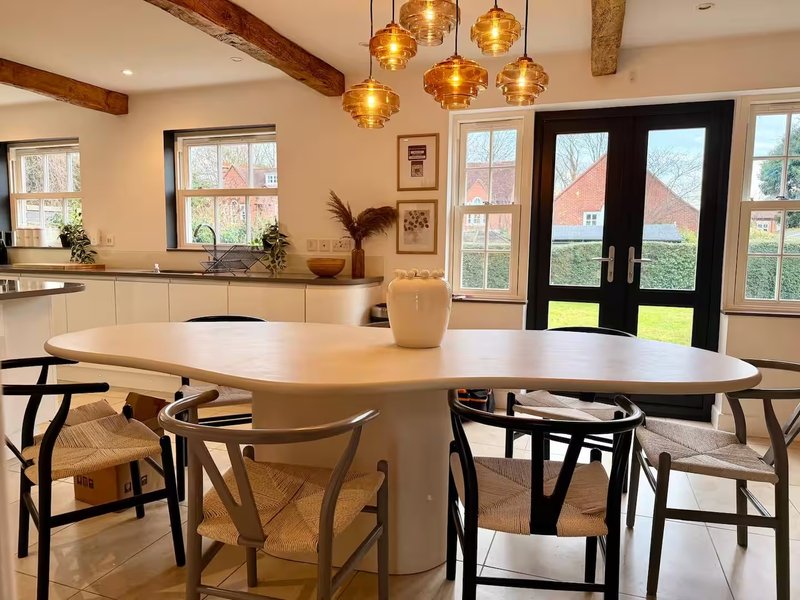 Open-plan kitchen and dining area with oval white table, wooden chairs, pendant lights, and garden views