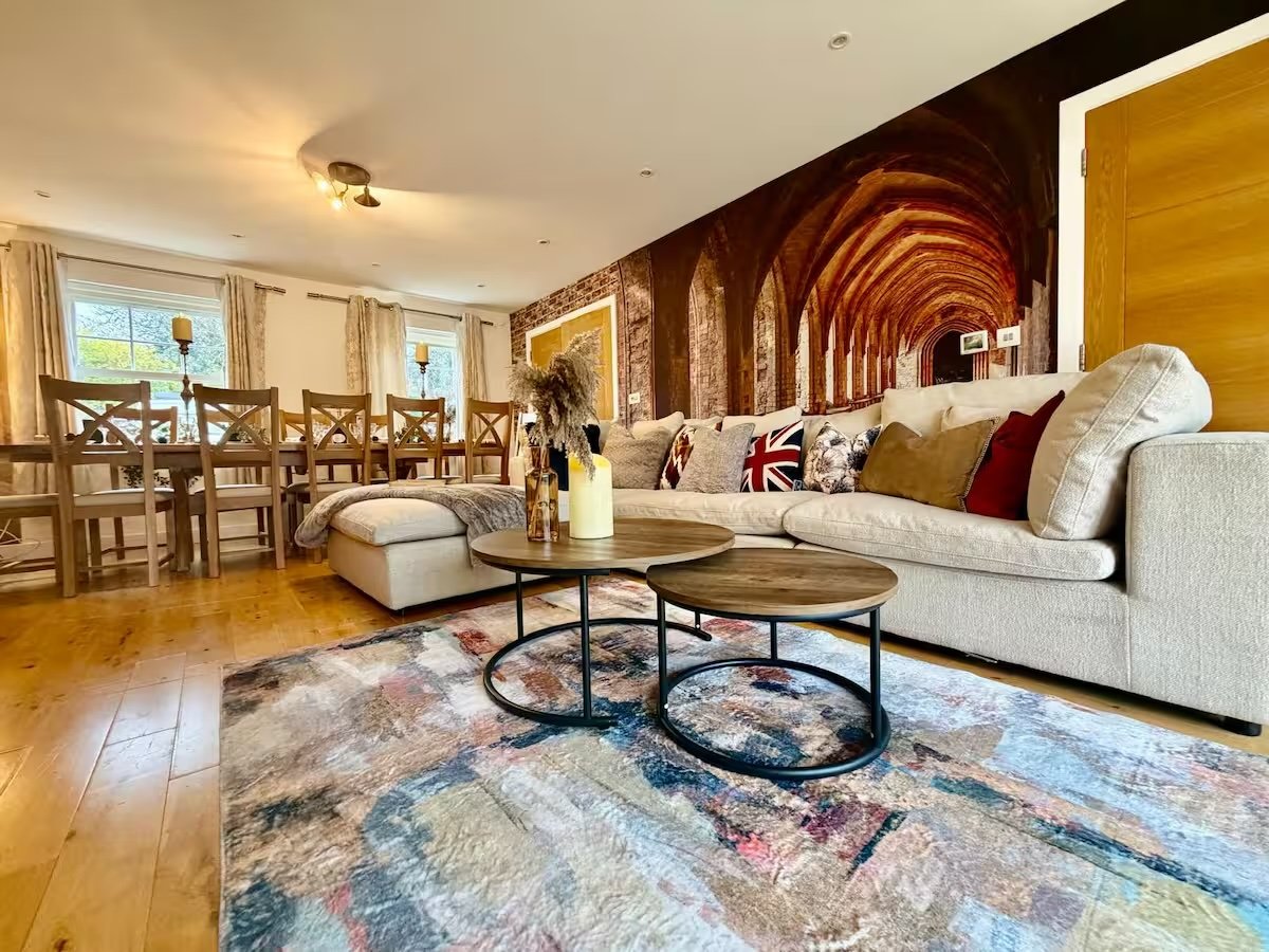 Open-plan living room with cream sofa, wooden dining table, circular coffee table, and archway wall mural