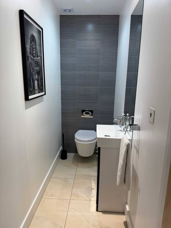 Modern bathroom with toilet, sink, grey tile wall, and framed artwork