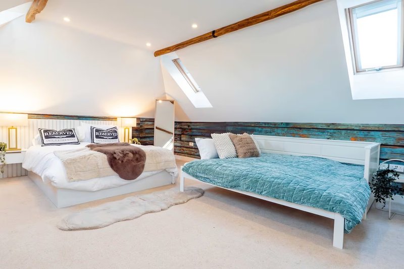 Bright attic bedroom with two beds, wooden beams, skylight windows and neutral décor