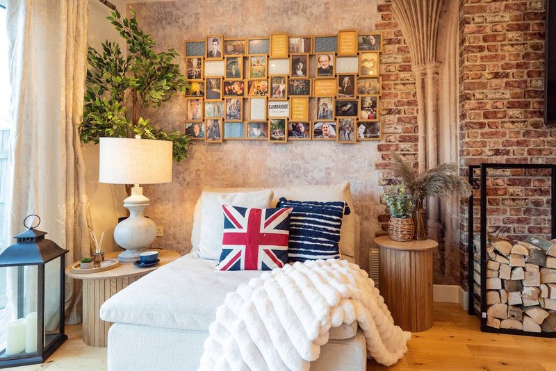 Bedroom with exposed brick walls, bed with white bedding, decorative photo gallery wall, fireplace with firewood storage
