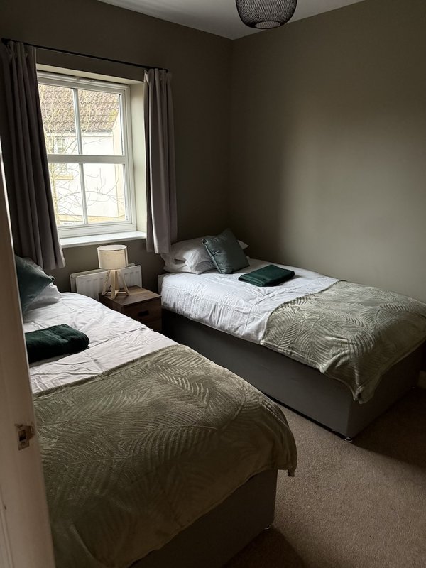 Bedroom with three single beds, olive bedding, window with grey curtains, ceiling light fixture