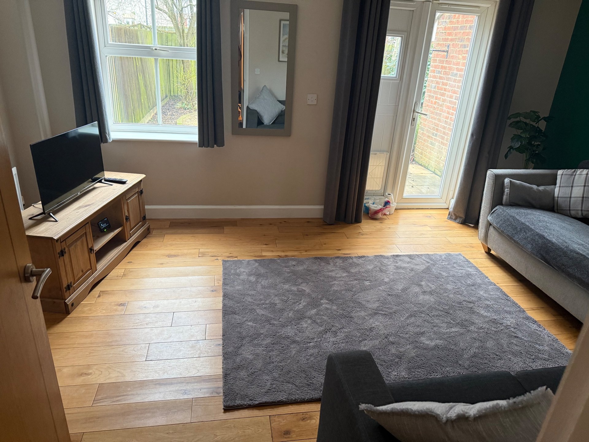 Bright living room with wooden floor, grey rug, TV stand, sofa and garden views