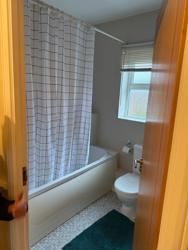 Bathroom with white tile shower curtain, bathtub, toilet, and window with blinds