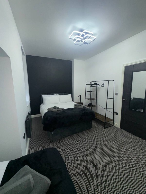 Modern bedroom with single bed, black accent wall, metal frame shelving and ceiling light