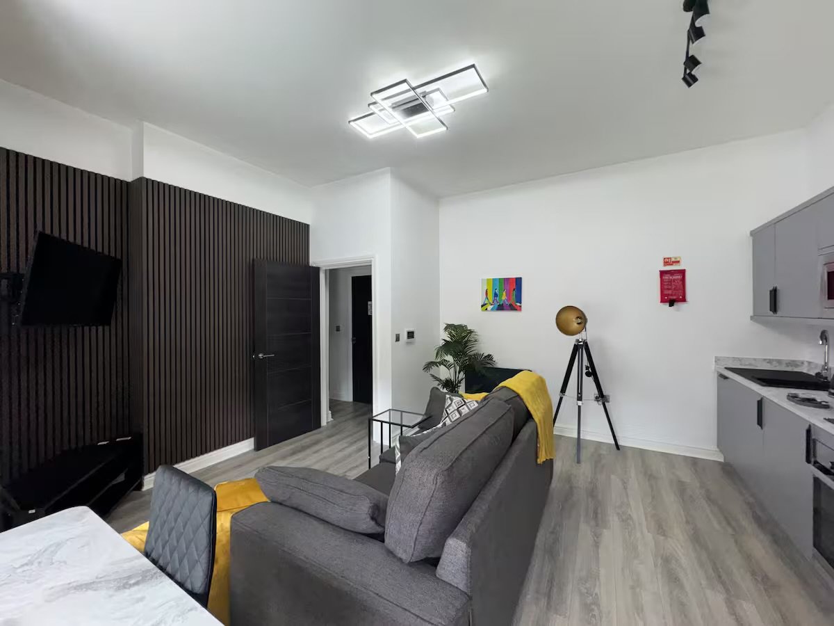 Open-plan studio with grey sofa, kitchenette, bed, and modern furnishings