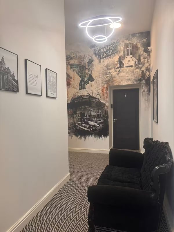 Modern hallway with neon planet sign, vintage city murals, framed prints, and black armchair