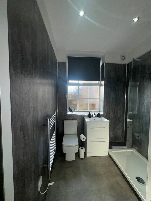 Modern bathroom with dark tile walls, toilet, sink, shower enclosure and window