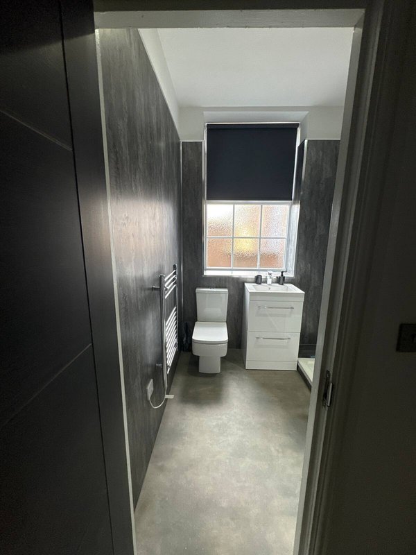 Compact bathroom with toilet, sink vanity, window and dark tile walls