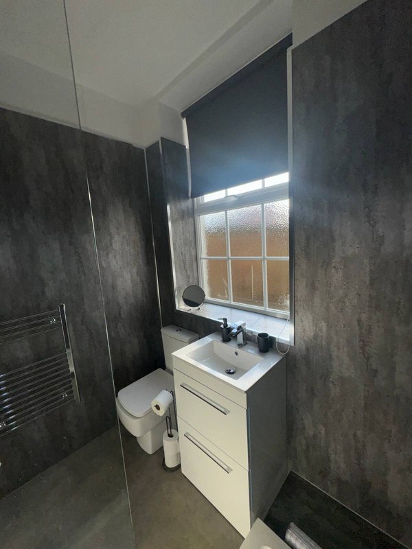 Modern bathroom with white vanity, sink, toilet, and dark tile walls