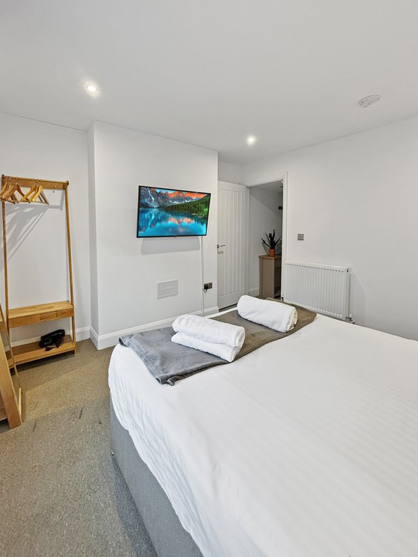 Bright modern bedroom with double bed, wooden clothes rack, wall-mounted TV, and radiator