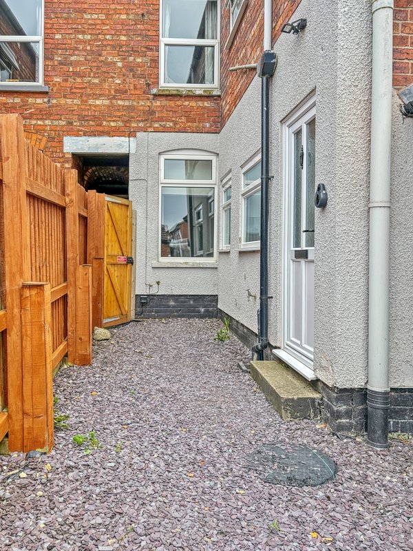 Side alley of brick and rendered houses with wooden gate and gravel ground
