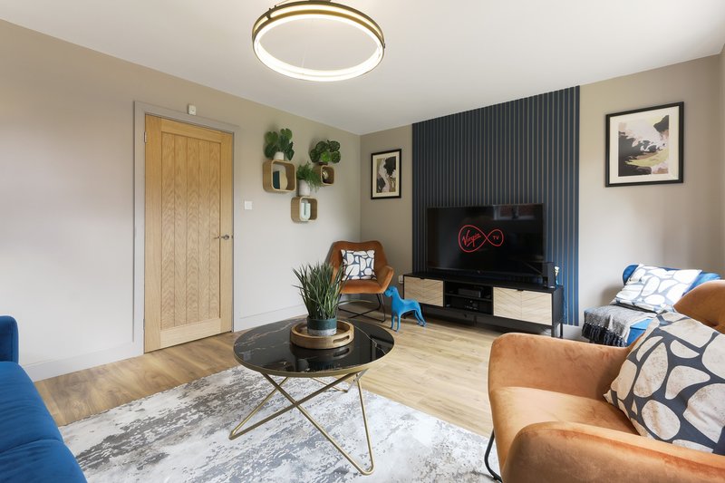 Modern living room with blue sofa, glass coffee table, wooden flooring and wall-mounted TV