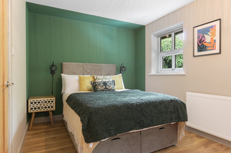 Bedroom with double bed, green accent wall, wooden nightstand and framed artwork