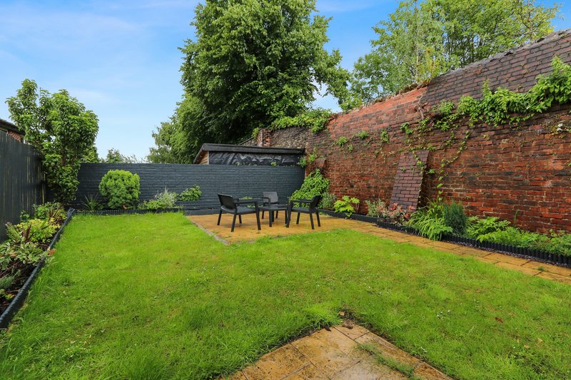 Garden with lawn, outdoor seating area, brick wall and mature trees