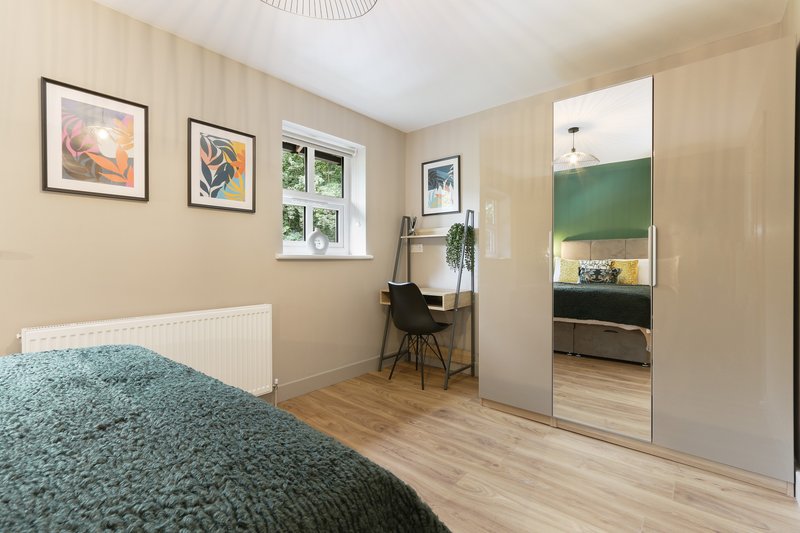 Bright bedroom with double bed, desk area, framed wall art, and mirrored wardrobe
