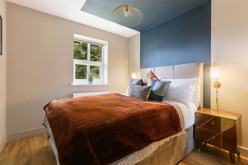 Modern bedroom with double bed, brown throw, blue accent wall, wooden nightstands and window