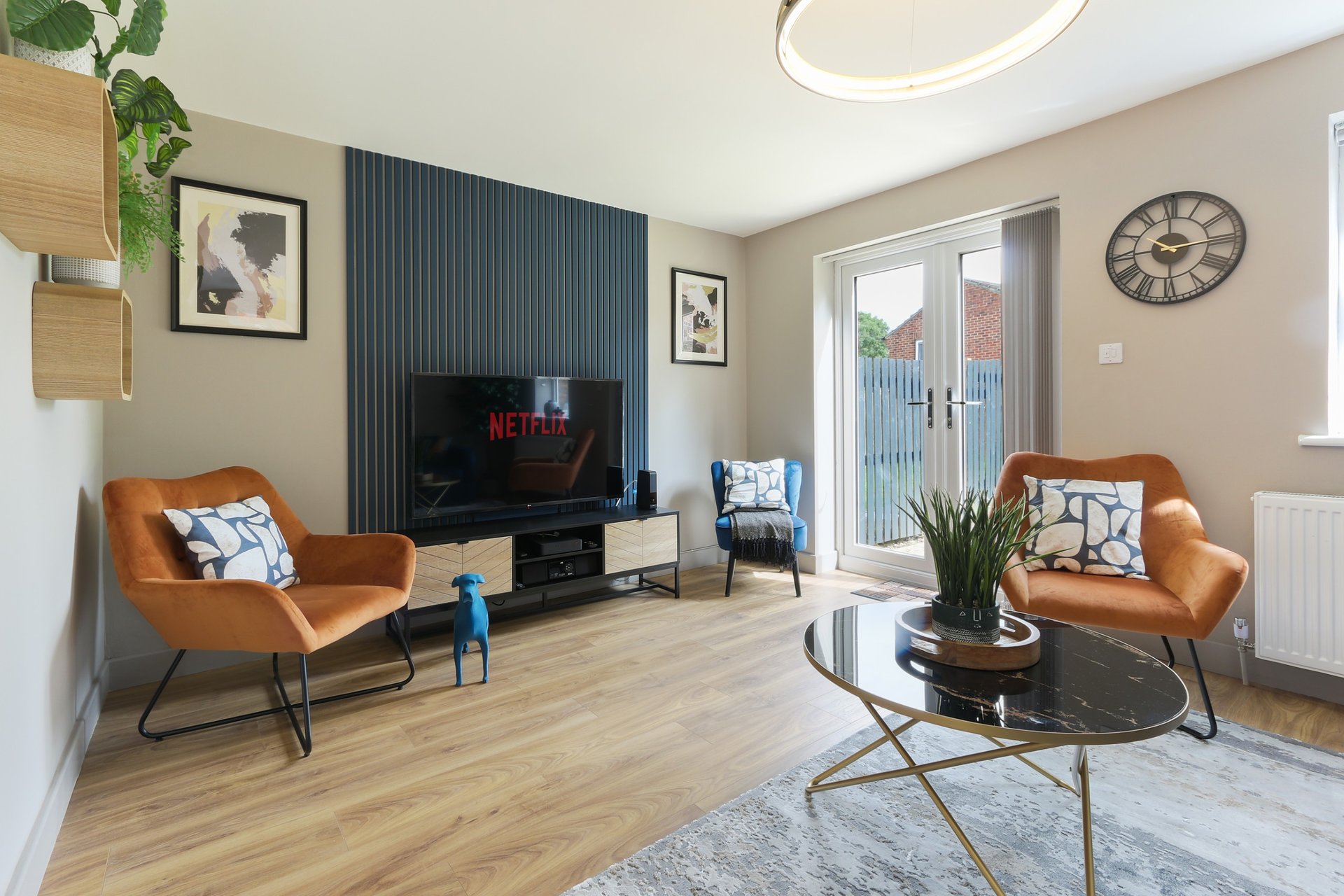 Modern living room with orange armchairs, TV, wooden flooring, and glass patio doors