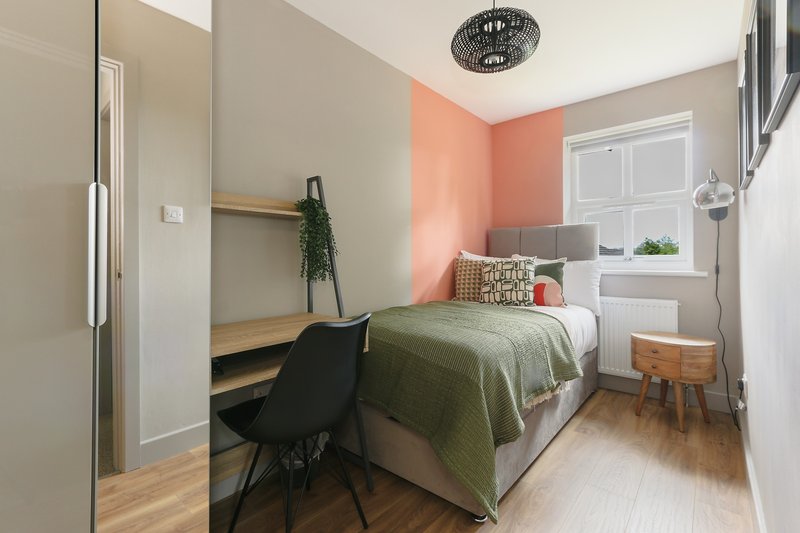 Compact bedroom with single bed, desk area, coral accent wall and wooden flooring