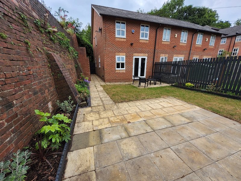 Brick terraced house with patio garden, black fence and green plants