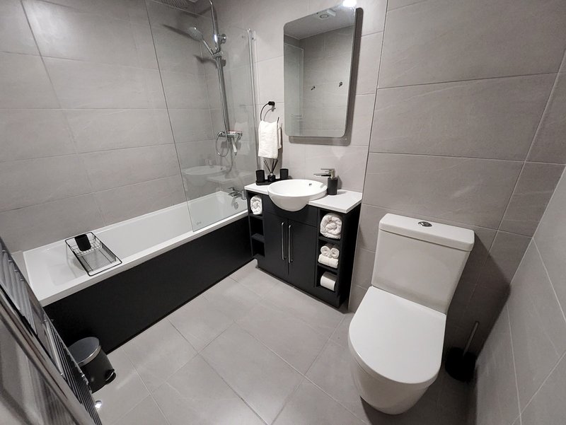 Modern bathroom with white toilet, black vanity unit, round sink, bathtub and shower enclosure
