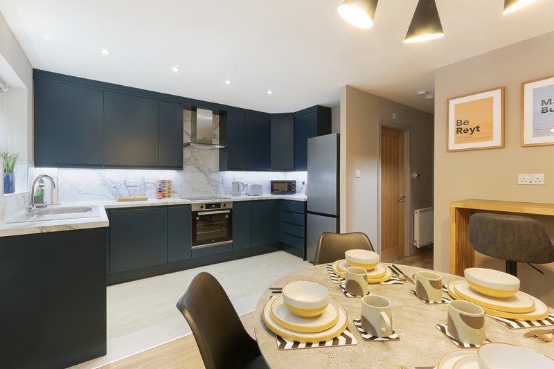 Modern kitchen with dark cabinetry, white countertop, and dining table set with yellow accents